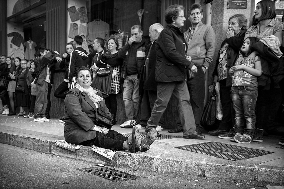 Personas esperan sentadas y de pie en una acera.